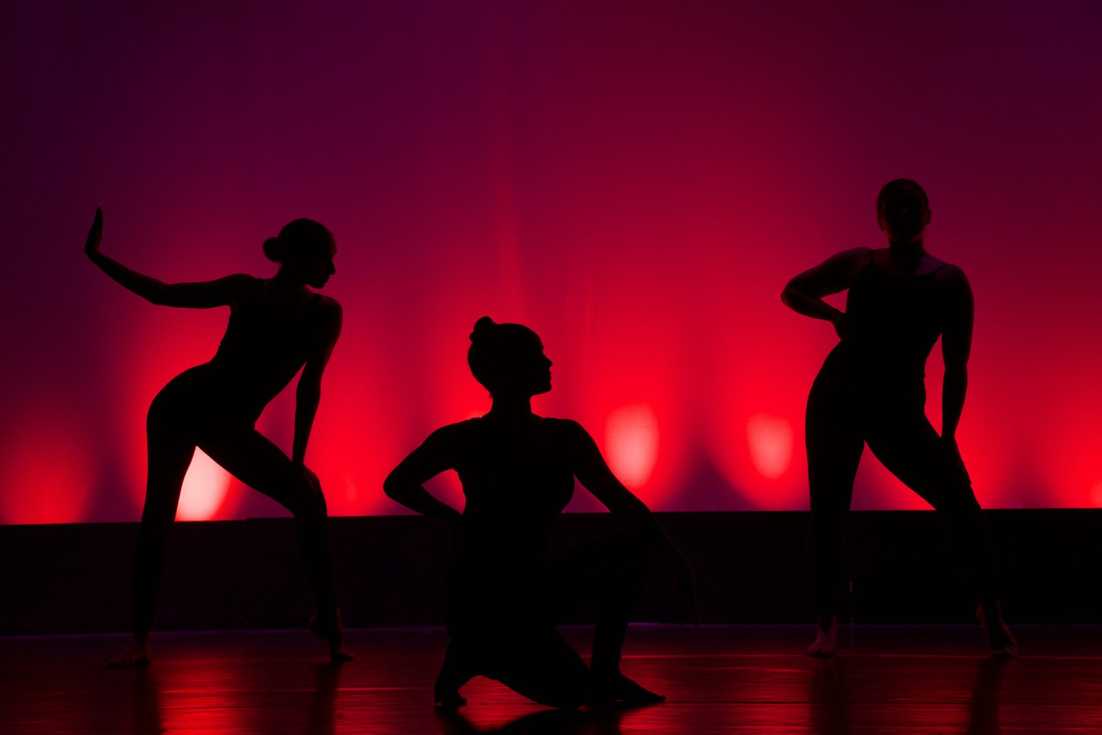 Silhouette de danseurs sur scène, éclairage rouge dramatique
